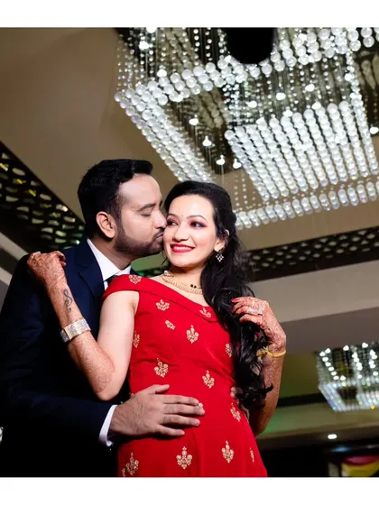 A classic reception photo, with the groom giving his bride a gentle kiss on the cheek. The opulent chandelier adds a touch of luxury to the scene.