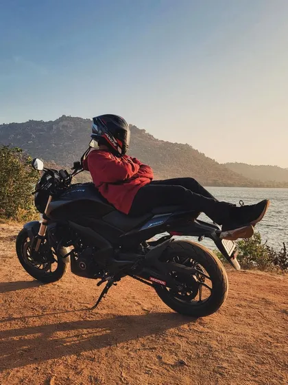 Taking a break on the county roads. A rider relaxing on his bike, parked by a lake with hills in the background during a sunset ride.