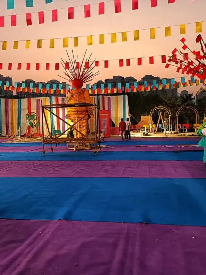 This image shows a large festival ground during the setup phase. You can see the scale of the event, with colorful carpeting laid out and various decorative structures being assembled before the event begins.
