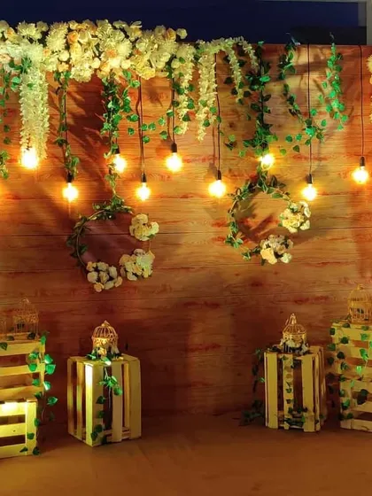 This rustic photo corner features a wooden pallet wall adorned with flowers, greenery, and hanging bulbs. We used illuminated wooden crates as decorative elements to complete the warm, inviting look.