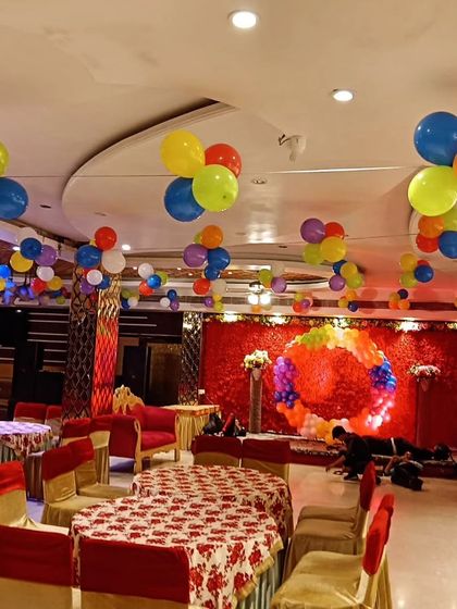 This image shows a banquet hall decorated for a birthday party. I used colorful balloon clusters on the ceiling and arranged the seating with printed tablecloths to create a fun party atmosphere.