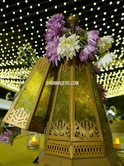 A close-up of a traditional centerpiece featuring a brass lantern and purple and white flowers. This element added a touch of cultural elegance to the reception tables.