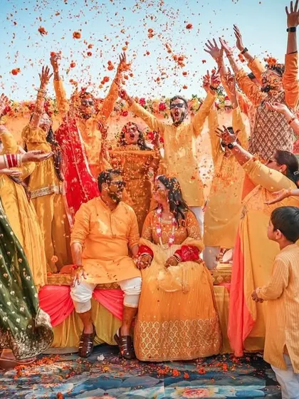 A wedding is about joy and celebration, and we capture every bit of it. This photo from a Haldi ceremony shows the couple surrounded by family and friends in a fun, candid moment of celebration, showering them with flower petals.