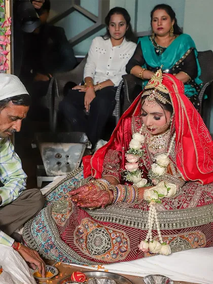 A candid photograph of the bride during the wedding puja. Her focus on the rituals, surrounded by ceremonial items, provides an authentic glimpse into the traditions and prayers that are central to a Hindu wedding.