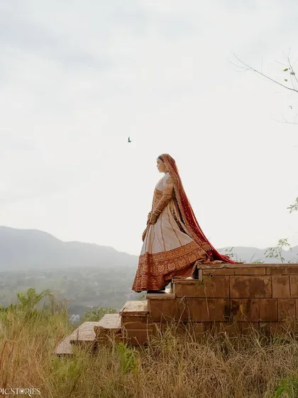 A breathtaking bridal portrait of Amruta. Standing atop the steps overlooking the hills, her long dupatta trailing behind her, she looks both powerful and serene against the vast landscape.
