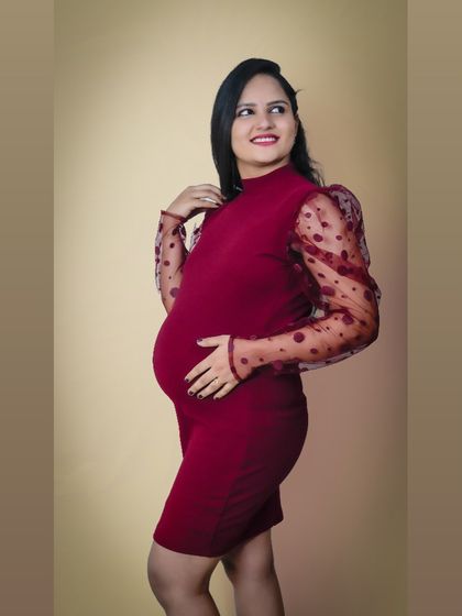 A modern and stylish studio portrait. The form-fitting red dress with sheer polka-dot sleeves is a chic choice for a mom-to-be who wants a contemporary look.