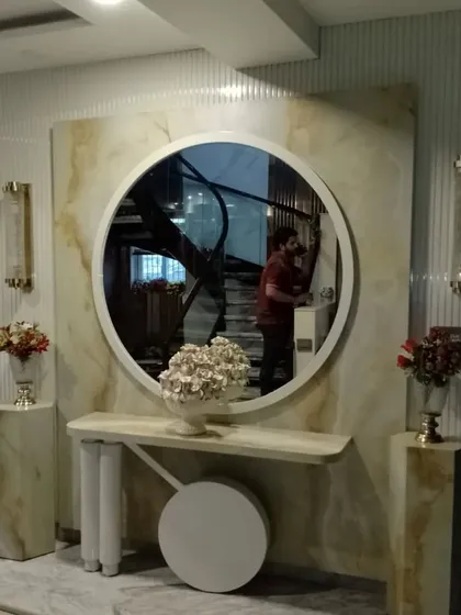 A luxurious foyer design featuring a statement wall of polished onyx. The large circular mirror, flanked by elegant wall sconces and pedestal vases, creates a grand and welcoming entryway.