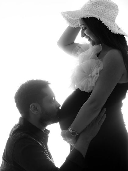 A beautiful black and white silhouette shot. The partner's kiss on the bump is a classic, tender moment, and the hat adds a touch of style.