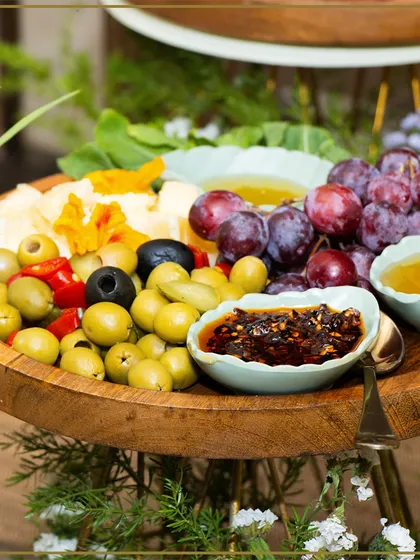 A wooden platter featuring a colorful assortment of olives, grapes, and dips. Our grazing boards are a feast for the senses.