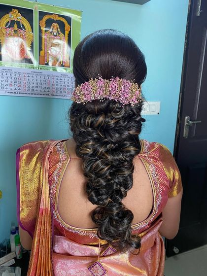 A voluminous messy braid with highlights, adorned with a custom pink floral accessory to match the client's saree.