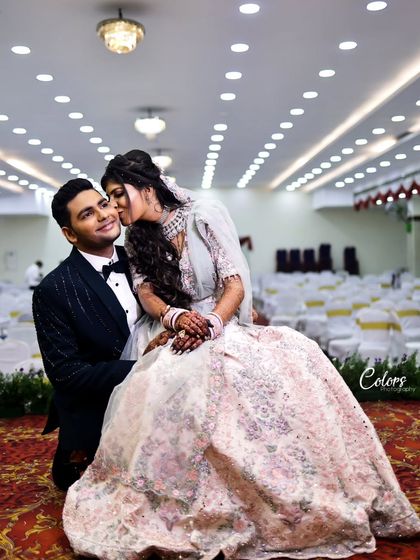 A playful and romantic shot where the bride kisses her groom's cheek in a grand, empty hall.