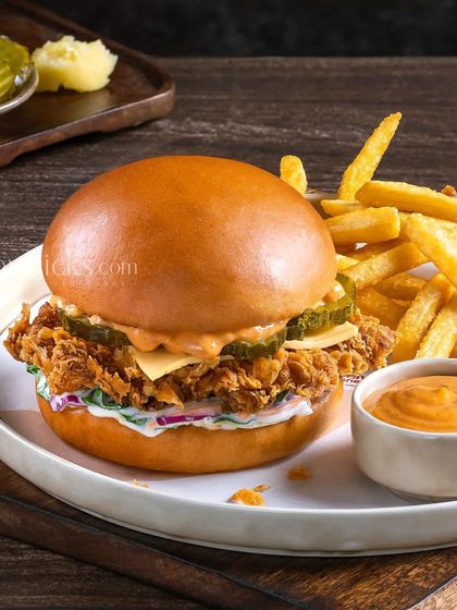 A crispy fried chicken burger with coleslaw and spicy sauce, served with a side of golden fries for a complete meal shot.