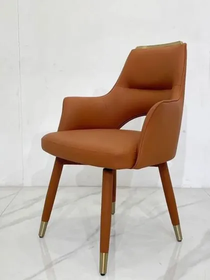 A modern dining chair in tan leatherette with gold-tipped legs. The open-back design adds a light, airy feel to your dining space.