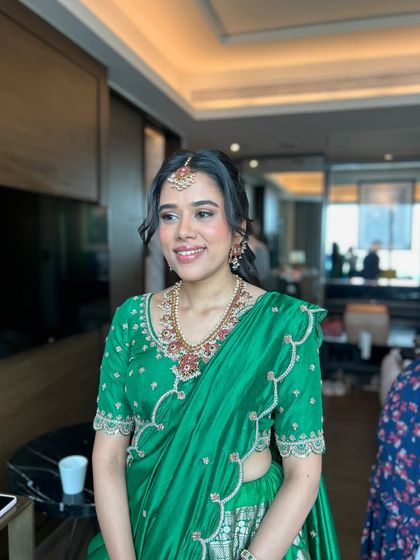 The bride looks radiant in her green saree, with soft tendrils framing her face and the half-bun adding a touch of modern elegance.