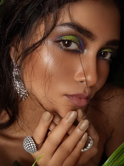 A close-up beauty shot with colorful, artistic makeup and statement diamond rings.