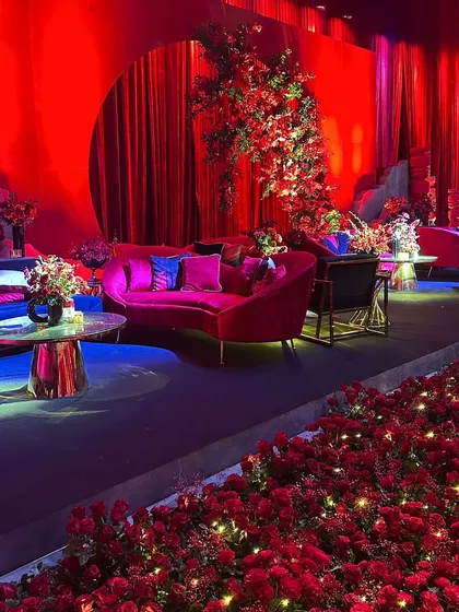 A close-up of a lounge area at the red-themed Sangeet, with a floral arrangement and a bed of roses illuminated by fairy lights, creating a magical and romantic detail.