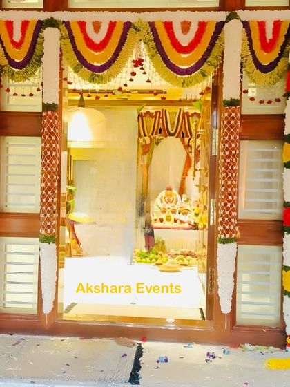 A full view of a decorated main door for a housewarming, with colorful floral garlands framing the entrance to the pooja room inside.