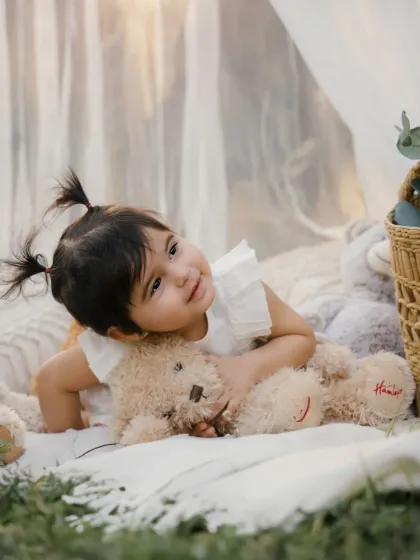 A close-up of a little girl with cute pigtails, hugging her teddy bear. A sweet and tender moment from her outdoor session.