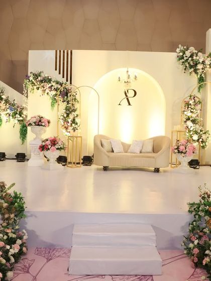 A chic and modern reception stage with asymmetrical floral arrangements on clean, white panels. The couple's monogram and golden arch details add a touch of personalized elegance to the minimalist design.