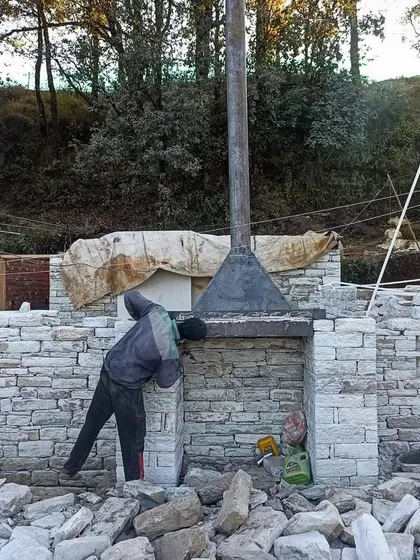 An artisan works on the interior of a stone fireplace, a central feature in our Himalayan homes. These fireplaces are designed to be both functional heat sources and beautiful focal points.