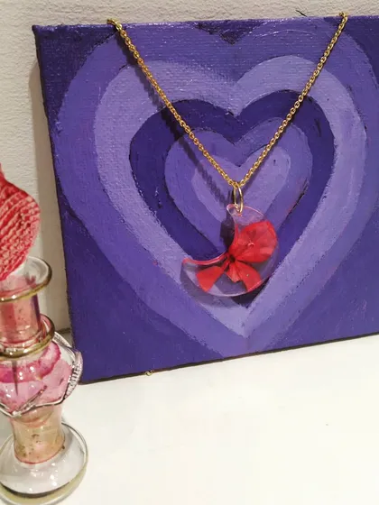 This crescent moon pendant holds tiny red flower petals. It's a delicate and romantic piece of wearable art.
