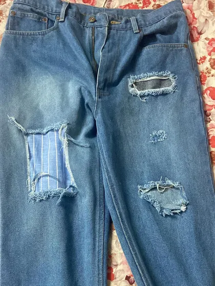 Custom ripped and repaired jeans. This pair features distressed areas and unique patches, including a striped fabric insert, for a personalized, worn-in style.