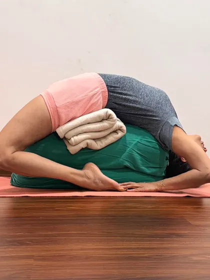 This is a supported Kapotasana (Pigeon Pose) using a bolster and blankets. Props allow the body to surrender into this intense backbend, releasing tension in the shoulders, chest, and hip flexors.