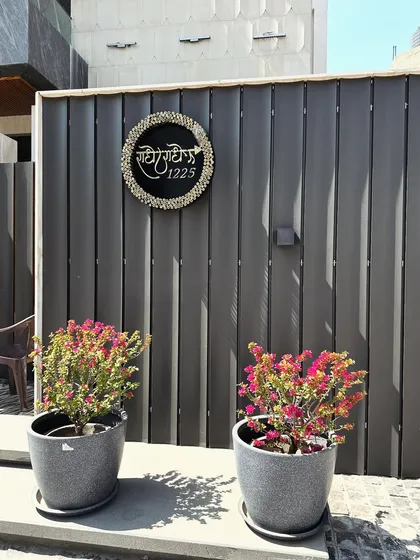 A custom nameplate on a modern slatted wall, flanked by two pots of vibrant bougainvillea, adding a personal touch and a splash of color.