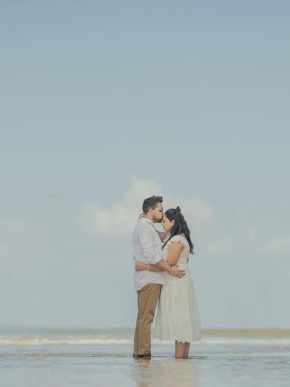 A wide, minimalist shot of a couple standing in the surf, emphasizing the tranquility and vastness of the ocean.