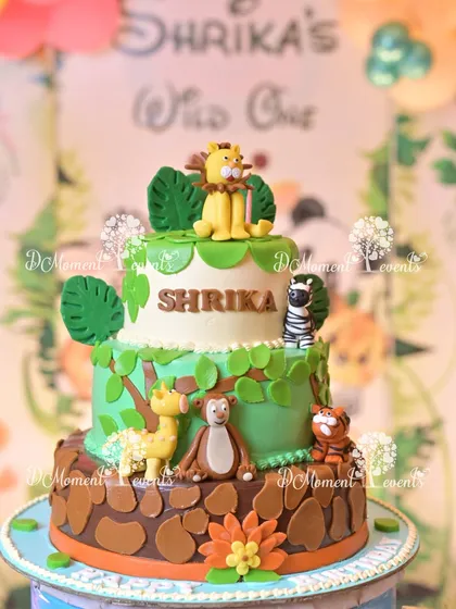 A stunning three-tiered jungle-themed cake, adorned with fondant animals like a lion, monkey, and giraffe, perfectly matching the "Wild One" party decor.