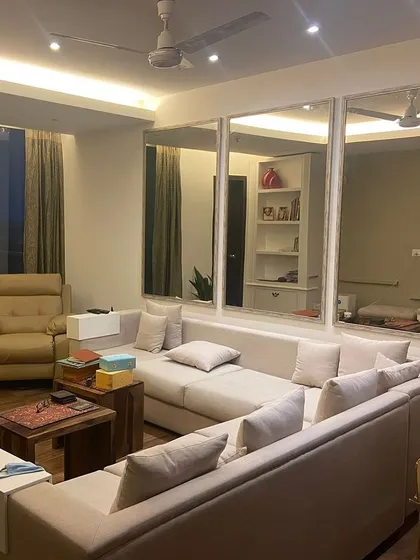 In this apartment living room, we used a large L-shaped sofa to maximize seating and comfort. The wall of oversized mirrors is a strategic design choice to amplify light and create a feeling of expansive space.