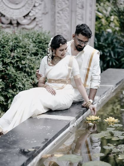 A serene and beautiful shot of a couple by a lily pond, the bride in a white Kerala saree, dipping her hand in the water.