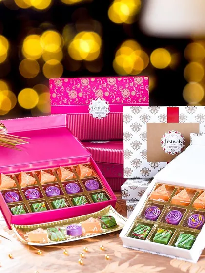 Two vibrant Diwali gift boxes filled with colorful Indian sweets, set against a background of glowing bokeh lights. This shot is full of festive magic and celebration.