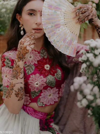 A beautiful close-up from a Mehendi shoot. The bride's intricate henna and the way she playfully peeks from behind a fan create a lovely, candid-style portrait that is full of charm.