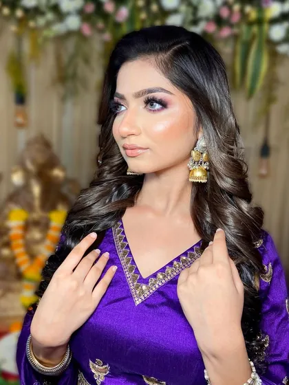 A stunning look featuring a vibrant purple outfit. The makeup is glamorous with a purple-toned smokey eye and beautiful, voluminous curls.