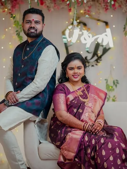 A stylish pose from the newly engaged couple. They sit back-to-back on a sofa, looking confident and happy against the festive floral and light decor.