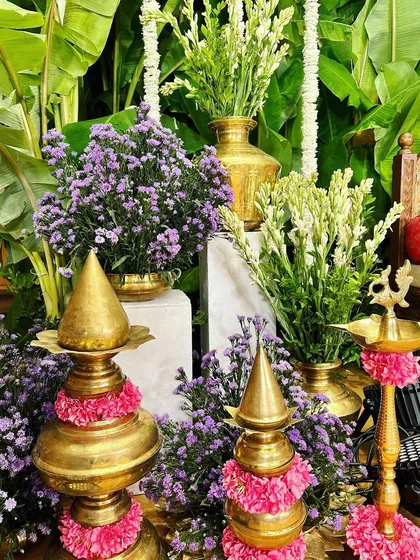 A collection of traditional brass decor, including lamps and kalashams, adorned with pink flowers, creating a rich and auspicious setting.