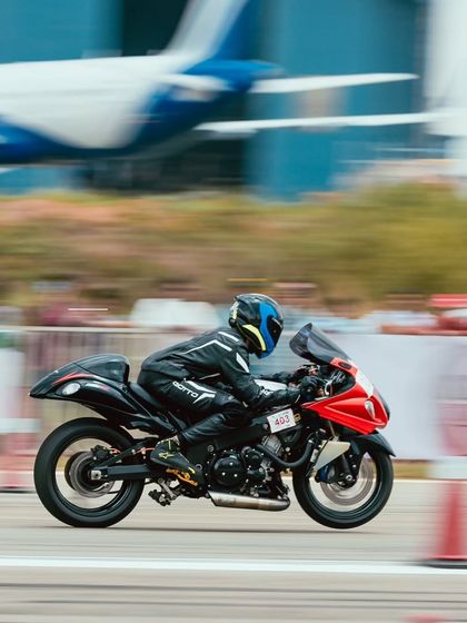 A rider on a modified motorcycle speeds past a parked airplane, a unique backdrop for our races at the Taneja Aerodrome.