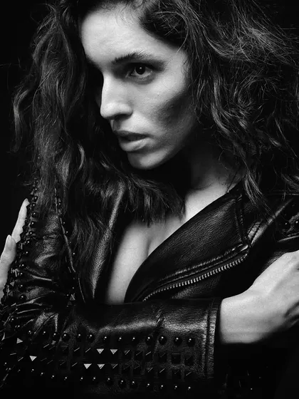 A close-up portrait in black and white. The lighting is carefully sculpted to create deep shadows and bright highlights, emphasizing the texture of the leather jacket and the intensity in her eyes. This is what I call grit.
