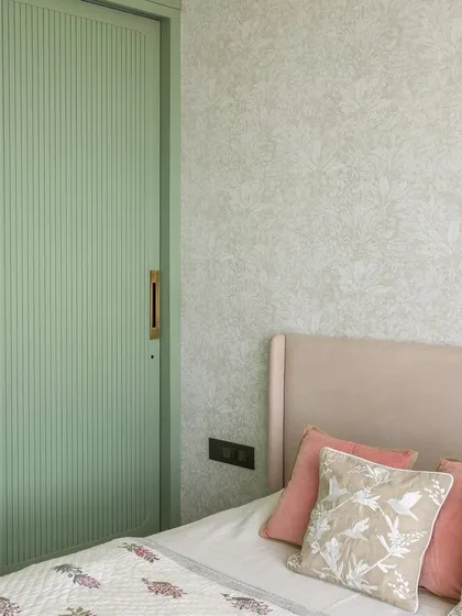 A detail from the bedroom, where a soft mint green fluted wardrobe door adds a gentle pop of color. This is paired with a delicate floral wallpaper and pastel pink cushions for a soft, romantic feel.