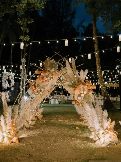 The entrance to the Mehendi night, an archway of pampas grass and dried florals illuminated by string lights, creating a magical, whimsical pathway for guests.