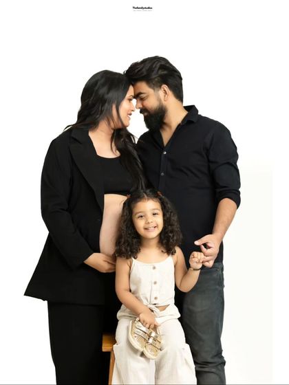 A modern studio maternity shoot with the whole family. The parents-to-be share an intimate moment while their daughter smiles at the camera, excited for her new sibling.