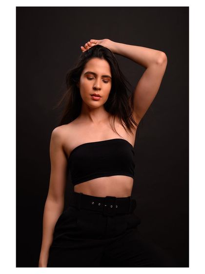 A minimalist and modern fashion portrait. The simple black outfit and dark background create a sleek and sophisticated look.