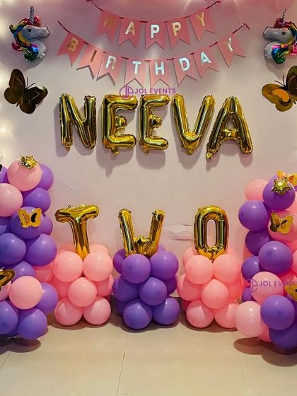 A cute unicorn and butterfly theme for a second birthday. The setup includes balloon pillars, foil letters for the name 'NEEVA' and the word 'TWO', and a 'Happy Birthday' banner.