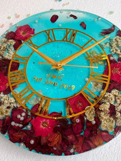 A full view of the vibrant turquoise and red flower clock. The scattered pearls and gold Roman numerals add a touch of luxury.