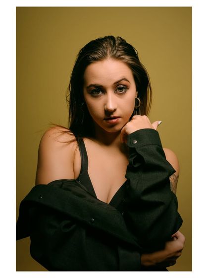 A moody and intense portrait with a dark, olive-green background. The lighting is focused on the model's face, creating a dramatic and captivating image.