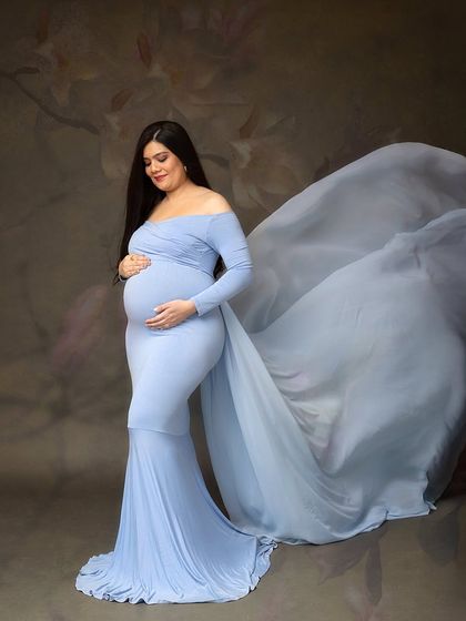 A gentle, downward glance at her baby bump. The soft folds of the light blue gown create a beautiful, cascading effect.