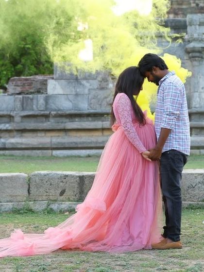 An intimate moment captured with a dramatic smoke effect in the background. The flowing pink maternity gown adds to the dreamy and romantic atmosphere of the shot.