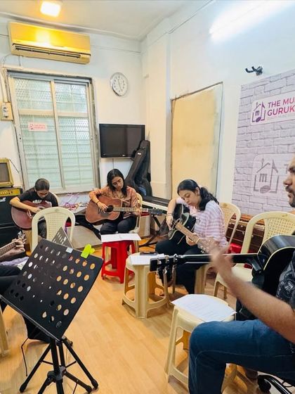 A coach leads a group guitar class, providing instruction and guidance. The setup with music stands and focused students is typical of our structured learning environment.