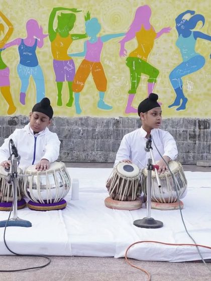 A focused shot of two young students playing tabla in unison during a public performance.